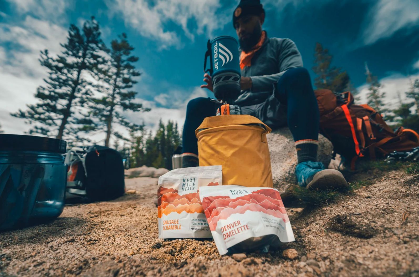 a man sitting on top of a rock cooking two Next Mile Meals Breakfasts