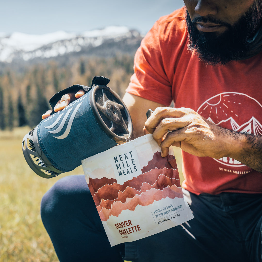 a man pours hot water into a backpacking meal