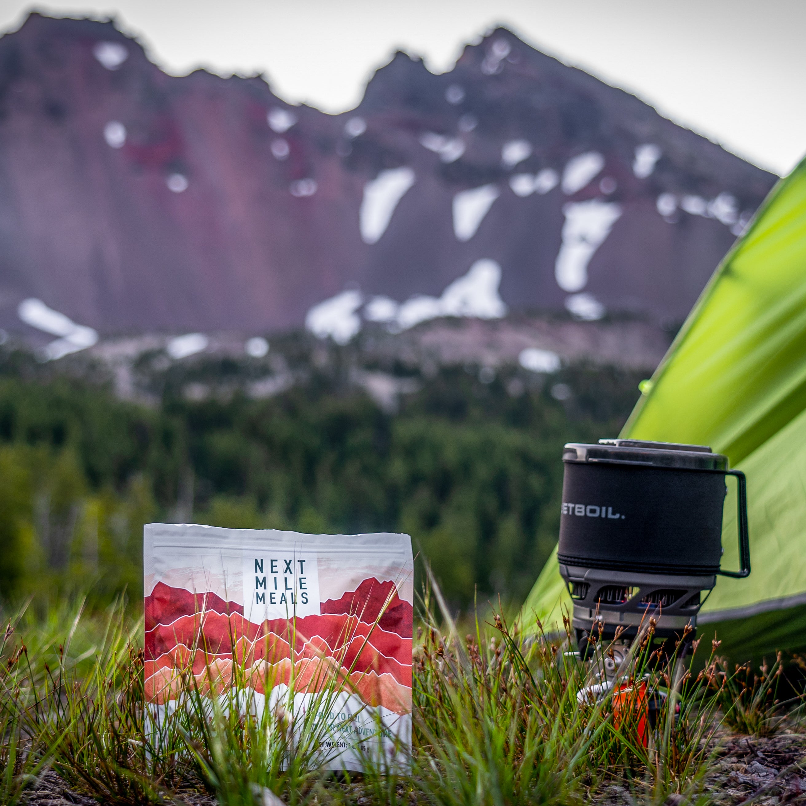 A backpacking meal sitting in the grass next to a tent.