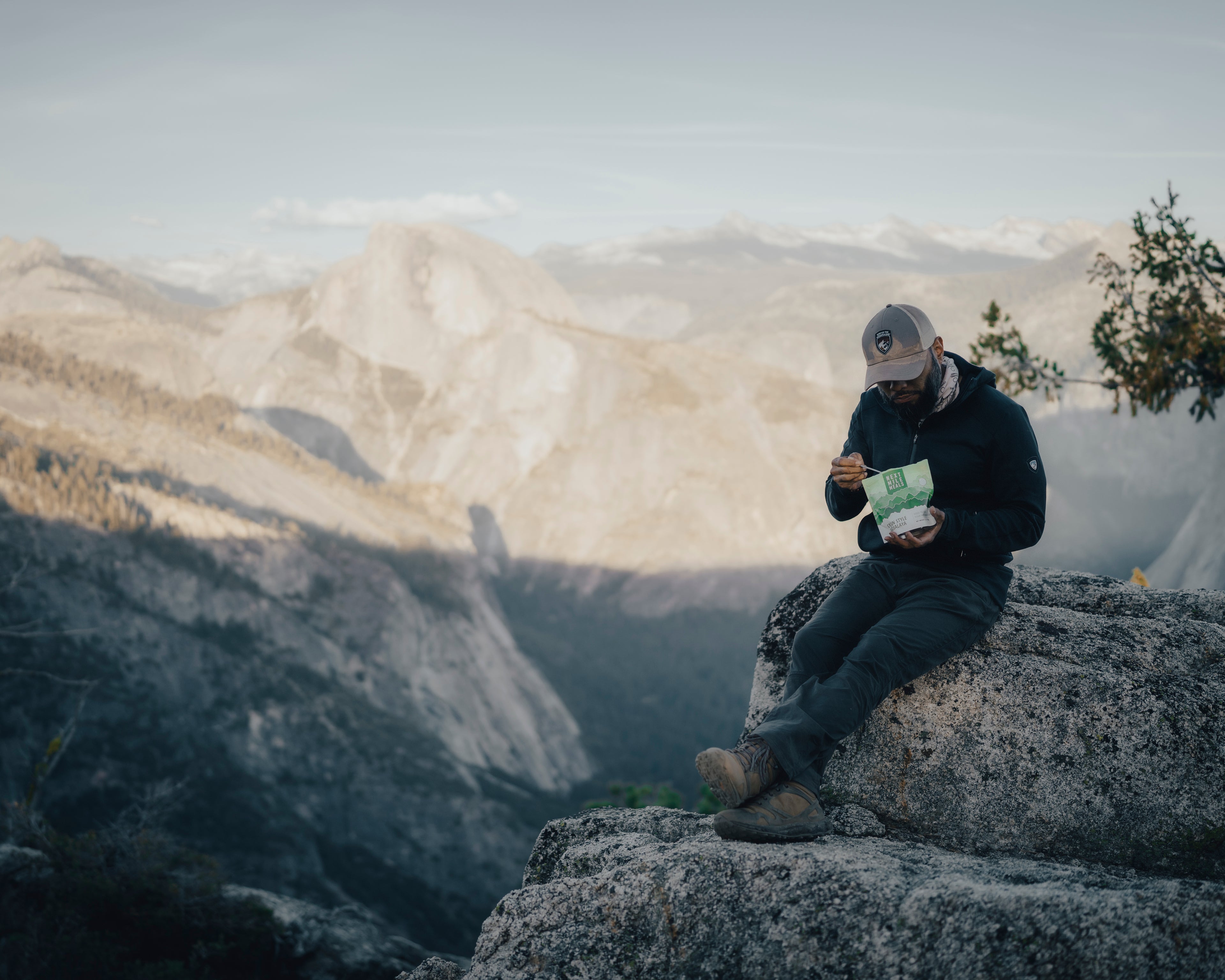 a man eats a backpacking meal while sitting on the edge of a cliff in Yosemite