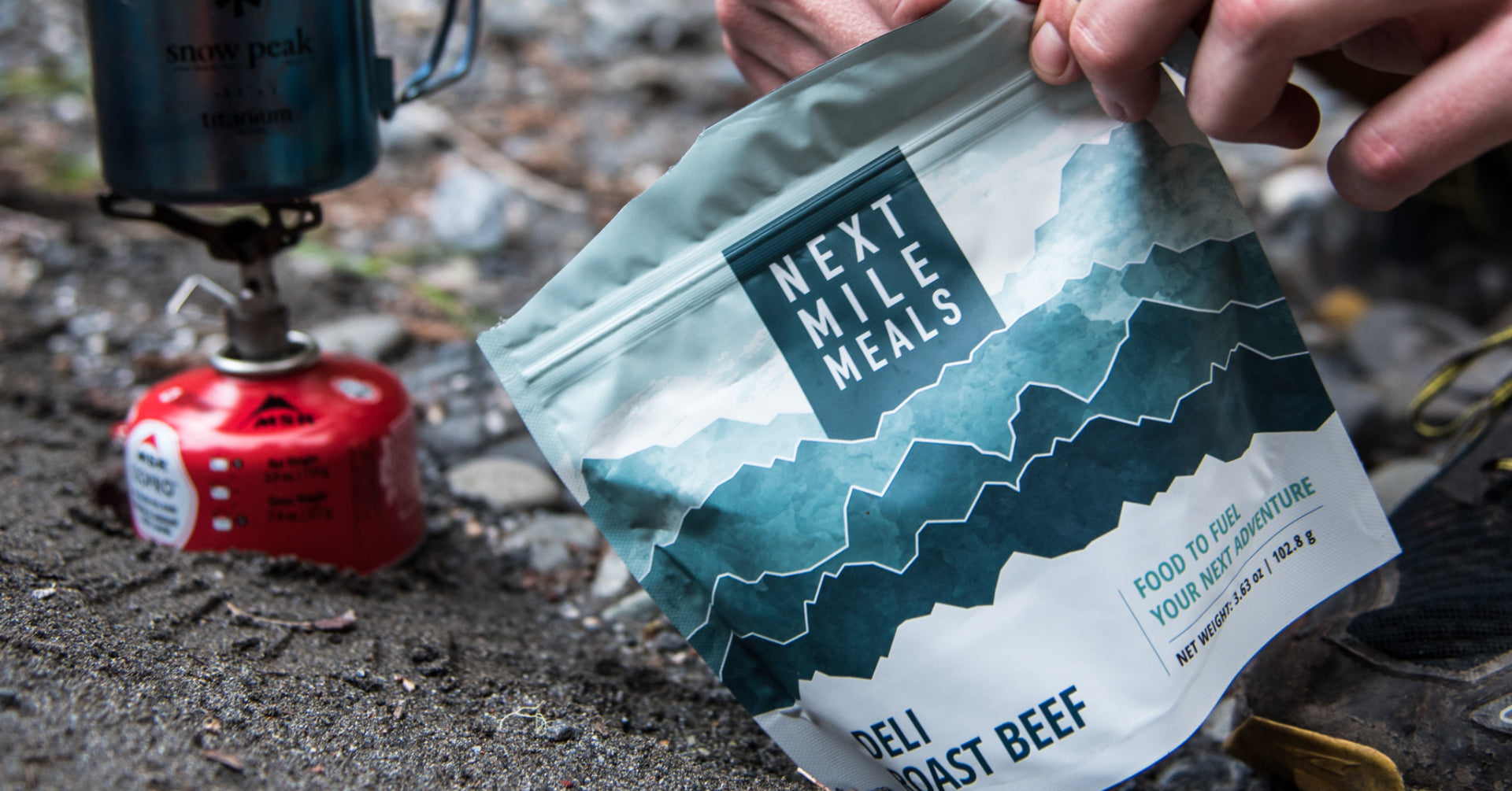 A backpacking meal being opened next to a camping stove